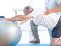 Physiotherapist helping man with exercise ball